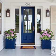 two blue planters with pink flowers are on the front porch of a white house