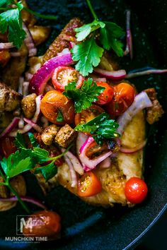 a pan filled with meat and vegetables on top of a black plate, topped with cilantro