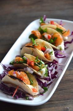 some tacos are on a white plate with red cabbage slaw and garnish