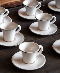 several white cups and saucers sitting on top of a wooden table next to each other