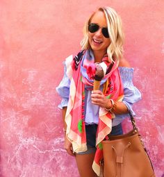 a blonde woman holding a brown purse and wearing a pink scarf with an ice cream cone in her hand