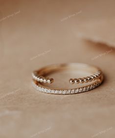 two gold rings with white stones on top of each one, sitting on a beige surface