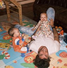 a man laying on the floor holding a baby and two other babies in front of him