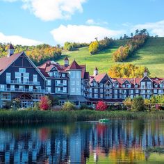 a large building sitting on top of a lush green hillside next to a lake filled with water