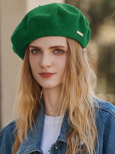 a woman with long blonde hair wearing a green hat and denim jacket, looking at the camera