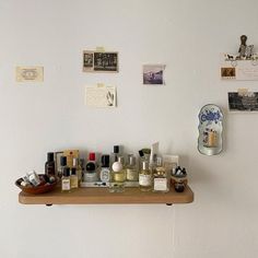 a wooden shelf with bottles on it in front of a white wall and several pictures