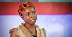 a woman with a head scarf on standing in front of a screen and looking off to the side