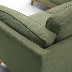 a green couch sitting on top of a white floor next to a wooden leg chair