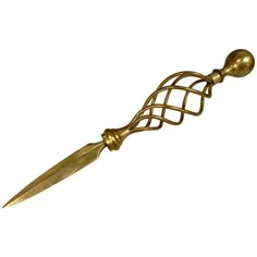 a gold colored metal object with a long blade on it's end and an intricate design in the middle