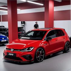 a red car parked in a garage next to two other cars and a man standing behind it