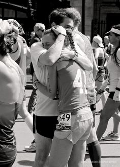 black and white photograph of two men hugging each other in front of runners on the street