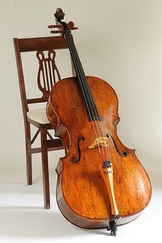 an old violin sitting on top of a wooden chair next to a string instrument in front of a white background