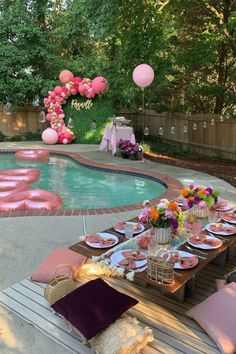 an outdoor pool party with pink balloons and plates on the table next to the pool