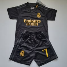 a black soccer uniform with gold lettering on the chest and shorts, which reads emirates fly better