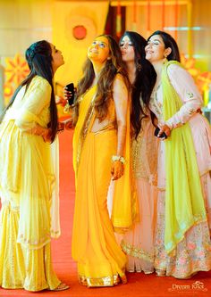 three women dressed in yellow and pink posing for the camera with one woman wearing an orange sari