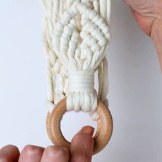 a person holding a wooden ring with white yarn on it and the rope attached to it