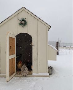 a chicken coop in the snow with its door open and two chickens standing inside it