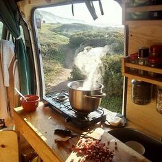 a kitchen area with a stove, pot and utensils on the counter in front of an open window