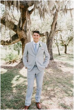 a man standing in front of a tree wearing a gray suit and tie with his hands in his pockets