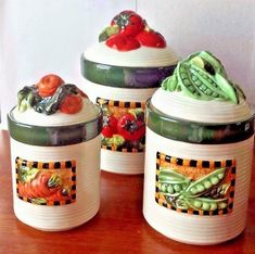 three canisters with vegetables painted on them sitting on top of a wooden table