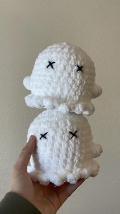 two white crocheted sheeps with black eyes are held up in front of the camera