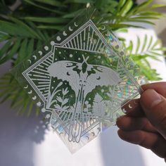 a person holding up some cut outs in front of a potted plant with green leaves