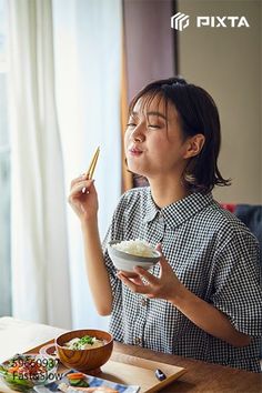 a woman sitting at a table eating food with chopsticks