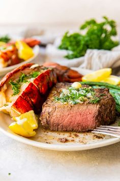 a plate with steak, lobster and lemon wedges on it next to some greens