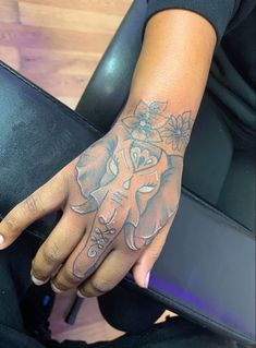 a woman's hand with an elephant and flowers tattoo on her left arm, sitting in a chair