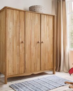 a wooden cabinet sitting next to a window in a room with wood floors and furniture