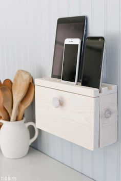 two cell phones sitting on top of a wooden shelf next to a cup and spoon