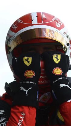 a man in a racing suit covering his face with two gloves and wearing a helmet