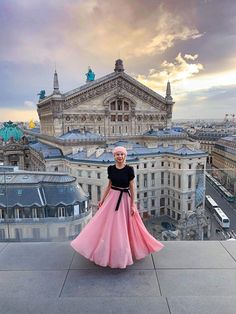 a woman standing on top of a building wearing a pink and black dress with her hands in her pockets