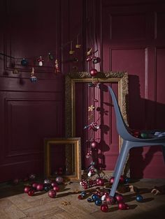 a chair sitting in front of a red wall with christmas ornaments on the floor next to it