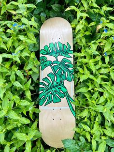 a skateboard with a plant painted on it is laying in the grass next to some bushes