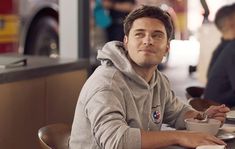 a man sitting at a table with a cup of coffee in front of him and looking off into the distance