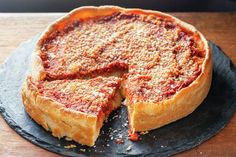 a deep dish pizza on a slate platter with one slice cut out and ready to be eaten