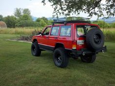 a red jeep parked on top of a lush green field