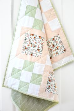 two quilts hanging on the side of a white door with green and pink squares