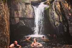 people are swimming in the water near a waterfall