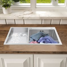 a kitchen sink that is open with clothes in the bottom drawer and next to it are potted plants