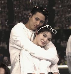 two people are hugging each other in front of an audience at a sporting event, one is wearing sunglasses and the other has her arms around his neck