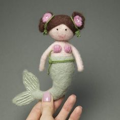 a hand holding a needle - felt mermaid doll in it's right hand, on a gray background