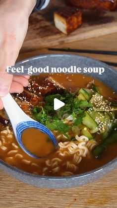 a bowl of soup with noodles and vegetables being spooned into it by someone's hand