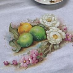 a painting of fruit and flowers on a table with a white plate in the background