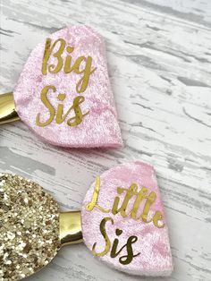 two pink and gold glitter hair clips with the words big sis, little sis on them