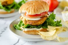 a chicken sandwich with lettuce, tomato and cheese on a plate next to chips