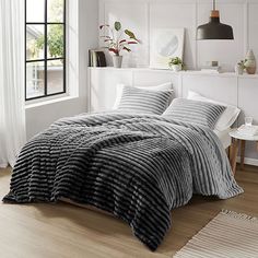 a bed in a bedroom with white walls and wooden floors, along with a black comforter