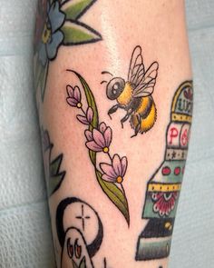 a close up of a person's leg with tattoos on it and a bee flying over flowers