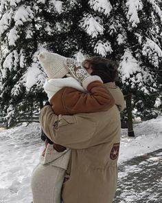 a woman holding a child in her arms while standing next to snow covered tree branches